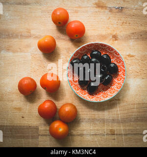 Kleine rote und weiße Schüssel mit Entkernten schwarzen Oliven und rote Tomaten auf einer hölzernen Schneidebrett. Quadratischen Format. Stockfoto