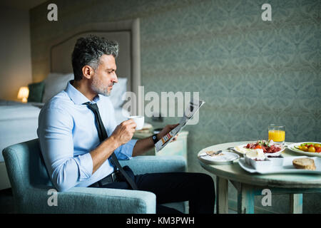Reifen Geschäftsmann mit Frühstück in einem Hotel Zimmer. Stockfoto