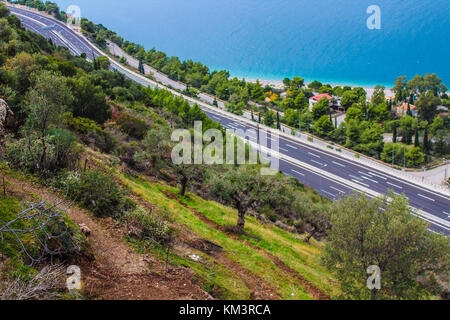 Olive Tree Feld auf einer Klippe mit Highway unter blauen Meer bunte griechische Landschaft und Stockfoto