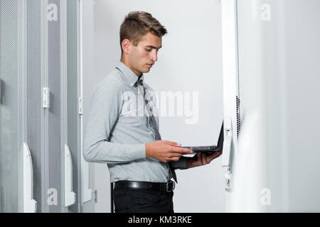 Portrait des modernen jungen Mann mit Laptop steht im Server Raum arbeiten mit supercomputer Stockfoto