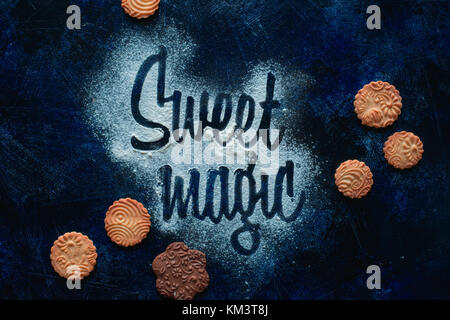Worte Sweet Magic mit Mehl. Cookies und Zucker Pulver auf einem dunklen Hintergrund. Essen Typografie Konzept. Süße flach. Stockfoto