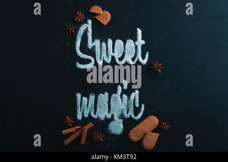 Worte Sweet Magic gemacht mit Zucker. Cookies und Krümel auf einem dunklen Hintergrund. Essen Typografie Konzept. Süße flach. Stockfoto