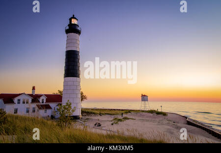 Lighthouse Beach Sonnenuntergang Hintergrund. Beleuchtete Big Sable Leuchtturm mit Leuchtturm auf dem sandigen Ufer des Lake Michigan bei Sonnenuntergang in Ludington. Stockfoto