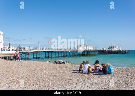 Junge Gruppe am Strand mit Worthing Pier hinter, Worthing, West Sussex, England, Vereinigtes Königreich Stockfoto