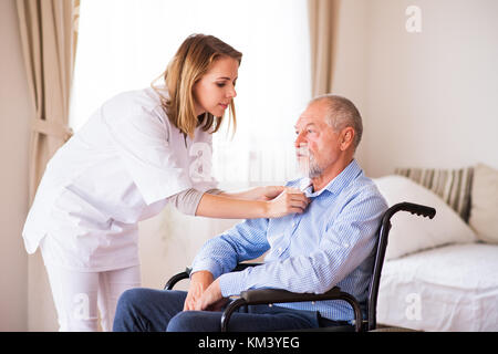 Krankenschwester und älterer Mann im Rollstuhl zu Hause besuchen. Stockfoto