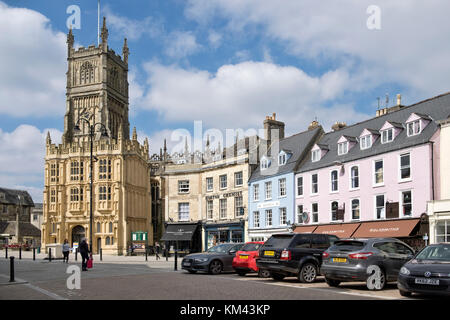 Den Marktplatz im Zentrum der Stadt Cirencester Gloucestershire, Vereinigtes Königreich. an einem sonnigen Tag, die Kirche des Hl. Johannes des Täufers. & Autos geparkt. Stockfoto