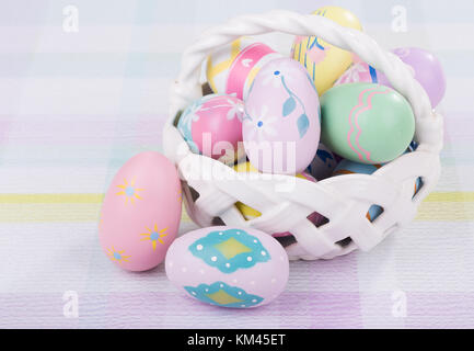 Bunt bemalte Ostereier und Korb auf einem pastellfarbenen Oberfläche Stockfoto