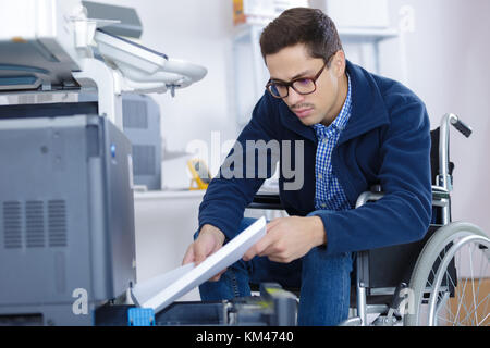 Mann im Rollstuhl setzt Papier so in den Drucker des Schrägförderers Stockfoto