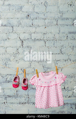 Baby rosa Kleid und rote Schuhe für das Mädchen, trocken auf einem Seil gegen eine weiße Wand. Stockfoto