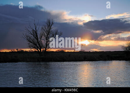 Ein Sonnenuntergang mit Regenwolken über dem Fluss Bure im Winter auf den Norfolk Broads in der Nähe von Horning, Norfolk, England, Großbritannien. Stockfoto