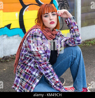 Attraktive junge Frau, die in Jeans und Plaid Shirt in die Kamera schaut im Sitzen. Stockfoto