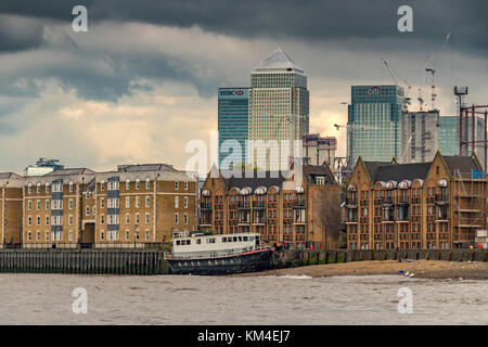 Großes Boot, das bei Ebbe an der Themse ankert, mit Apartments und Wohnungen am Fluss mit Blick auf die Türme von Canary Wharf, London und Großbritannien Stockfoto