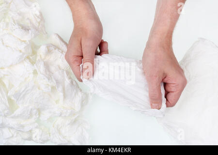 Ein älterer Mann trocknet und glättet schmutzig Papiertaschentücher für die Wiederverwendung auf weißer Tisch. Das Konzept der Armut. top View Studio shiot Stockfoto