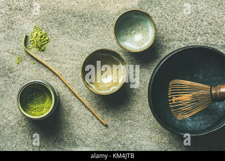 Flachbild-lay der japanischen Werkzeuge für die Zubereitung von Matcha Grüntee. matcha Pulver in Blechdose, chashaku Löffel, Chasen Bambusbesen, chawan Schüssel und Becher über Grau Stockfoto