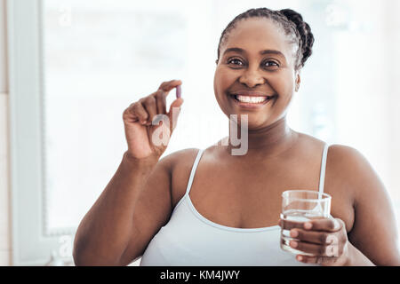 Lächelnd afrikanische Frau, die eine Pille und Glas Wasser Stockfoto