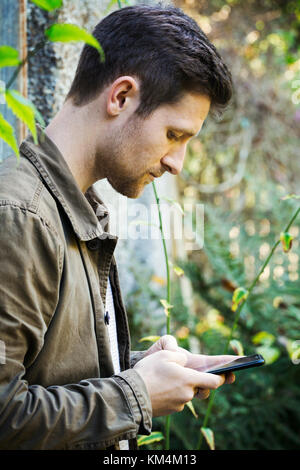 Ein junger Mann in einer braunen Jacke sms mit einem smart phone Stockfoto