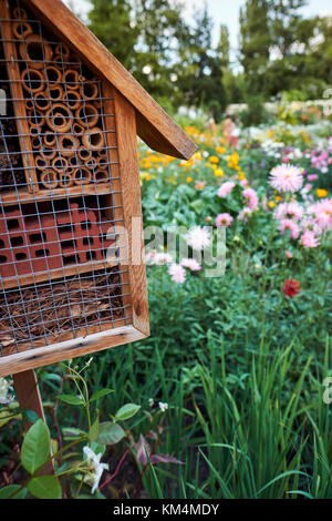 Ein Insekt Hotel, geeignet für eine Vielzahl von Insekten zu Nest oder Hibernate in einem Wildlife freundlich Garten, durch Pollen produzieren Blumen umgeben.