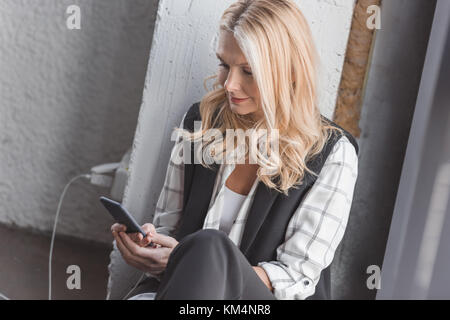 Lächelnd Geschäftsfrau laden Smartphone und das Sitzen auf dem Boden im Büro Stockfoto