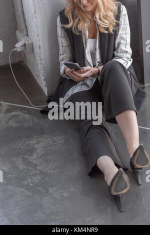 7/8 Schuß von lächelnden Geschäftsfrau Aufladen Handy und das Sitzen auf dem Boden Stockfoto