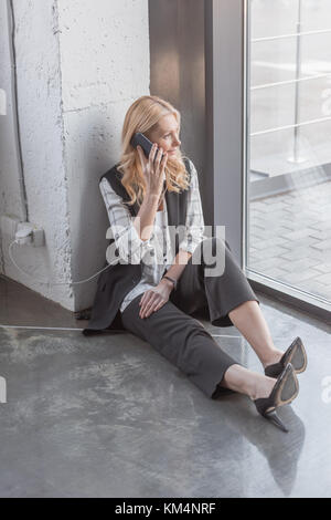 Geschäftsfrau laden Smartphone und Anruf beim Sitzen auf dem Boden im Büro Stockfoto