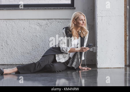 Schöne Geschäftsfrau laden Smartphone und das Sitzen auf dem Boden Stockfoto