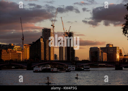 Blick auf die Skyline von London am Südufer der Themse mit von der untergehenden Sonne beleuchteten Gebäuden, Brücken und dem dunklen Fluss. Stockfoto