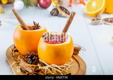 Weihnachten Glühwein - ungewöhnlich in Orange serviert. Heißer Winter trinken mit Beeren, Orangen, Gewürzen, Zimt auf den Holztisch mit Weihnachtsbaum Branc Stockfoto