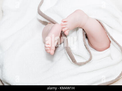 Baby Füße unter dem Handtuch. Baby in Windel liegen auf dem Bett, unkenntlich Baby. seichte doff. Nahaufnahme Bild von New Born Baby Füße auf ein weißes Blatt. Stockfoto