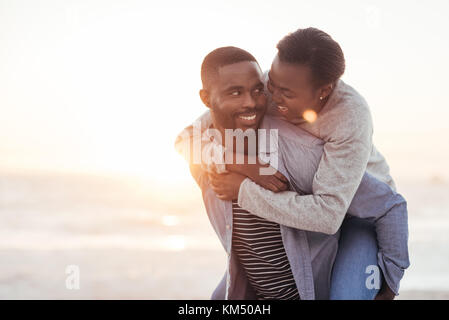 Junge Mann seiner Freundin ein Huckepack am Strand geben Stockfoto