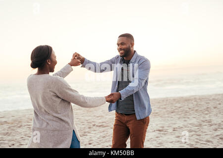 Unbeschwerte junge afrikanische Paar tanzen zusammen am Strand Stockfoto