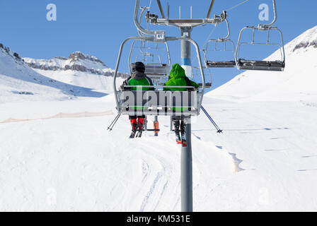 Zwei Skifahrer in grüne Jacke klicken Sie oben auf der Sesselbahn und verschneite Skipiste bei Sun winter Tag. Kaukasus, Georgien, Region Gudauri. Stockfoto