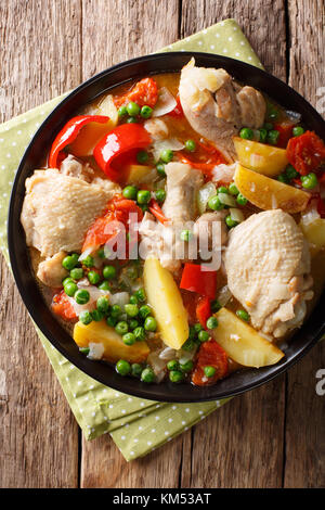 Stücke von Huhn Eintopf mit Kartoffeln, Paprika, Tomaten, Erbsen und Zwiebeln close-up in einer Schüssel auf den Tisch. Senkrechte Draufsicht von oben Stockfoto