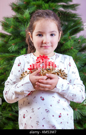 Frohe Weihnachten und Frohes neues Jahr. Lächelndes kleines Mädchen mit vielen Bändern für Weihnachtsbaumschmuck. Sie ist sehr, sehr glücklich Stockfoto