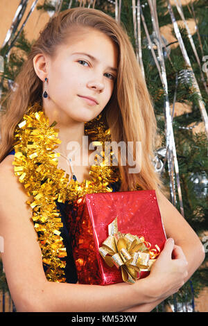 Ein frohes Schönes jugendlich Mädchen umarmt ihr Geschenk in der Nähe von einem Weihnachtsbaum Stockfoto