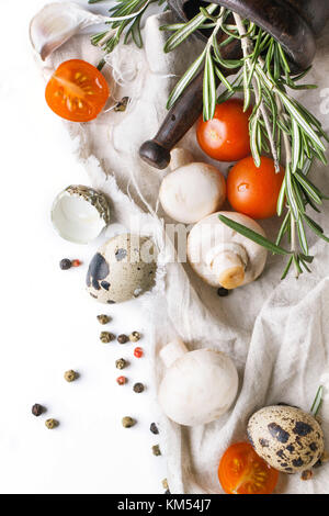 Ansicht von oben auf die wachteleier mit Champignons, in Scheiben geschnittene Tomaten und Rosmarin auf weißer Lappen über Weiß Stockfoto