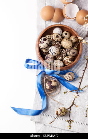 Ansicht von oben auf die hölzerne Schüssel von der Wachtel Eier mit Blüte Zweig und Eierschale über Weiß Stockfoto