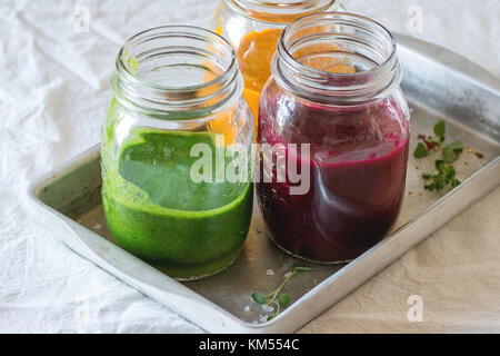 Jahrgang Fach mit Sortiment an Gemüse Smoothies aus Karotte, rote Beete und Spinat, die in Gläsern. über weiße Tischdecke. rustikalen Stil, Tageslicht Stockfoto