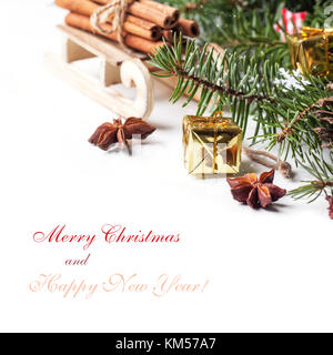 Weihnachtskarte mit hölzernen Schlitten mit Haufen von Zimt und goldenen Geschenkkarton über Weiß mit Mustertext Stockfoto