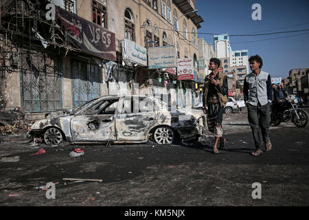 Sanaa, Jemen. Dezember 2017. Jemenitische Männer gehen an Autos vorbei, die bei Zusammenstößen zwischen Houthi-Kämpfern und Truppen des ehemaligen jemenitischen Präsidenten Ali Abdullah Saleh in Sanaa, Jemen, am 5. Dezember 2017 zerstört wurden. Saleh wurde am Montag von Huthi-Rebellen getötet. Quelle: Hani Al-ANSI/dpa/Alamy Live News Stockfoto