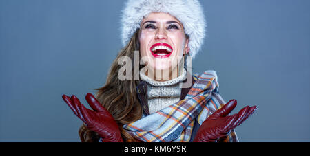 Wintersachen. Porträt von lächelnden trendige Frau in Pelzmütze isoliert auf kalten Blau Schneeflocken fangen Stockfoto