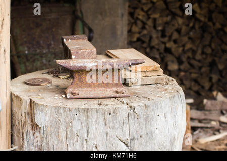 Eine alte Werkstatt Amboss auf einem grossen hölzernen stumpf Werkbank mit Holz im Hintergrund gestapelt behoben Stockfoto