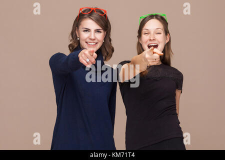 Frauen, die in der Nähe von einander und zeigen Sie mit dem Finger auf Kamera. studio Shot, hellbraunen Hintergrund Stockfoto