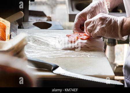 Männliche Hände stapeln Räucherlachs Schichten auf einem Tisch. Stockfoto