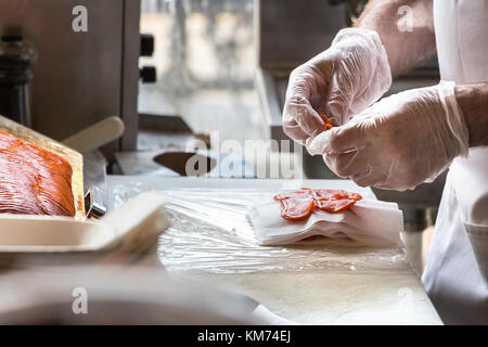 Männliche Hände stapeln Räucherlachs Schichten auf einem Tisch. Stockfoto