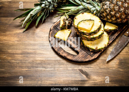 In Scheiben geschnittene Ananas auf einem Schneidebrett mit einem Messer auf einen hölzernen Tisch. Stockfoto