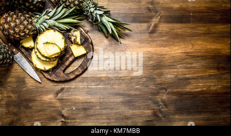 In Scheiben geschnittene Ananas auf einem Schneidebrett mit einem Messer auf einen hölzernen Tisch. Stockfoto