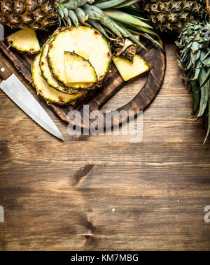 In Scheiben geschnittene Ananas auf einem Schneidebrett mit einem Messer auf einen hölzernen Tisch. Stockfoto