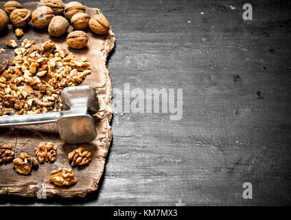 Zerkleinerte Walnüsse mit einem Hammer auf dem alten Board. Auf einer schwarzen Tafel Stockfoto