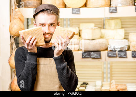 Lustige Porträt einer stattlichen Käse Verkäufer in Uniform stehend mit Käse vor dem Store Showcase voll von verschiedenen Käsesorten Stockfoto