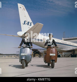 Die SAS DC-8 33, ein Flugzeugflugzeug aus den 1960er Jahren, wird am Boden in Dan Viking Lackierung gezeigt, wobei Bodendienste und Hostessen die Passagiere am Flughafen unterstützen. Stockfoto